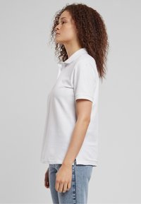 Hvid bomulds polo t-shirt med korte ærmer, en krave med tre knapper og en afslappet pasform. Bæres sammen med lyseblå denimjeans.