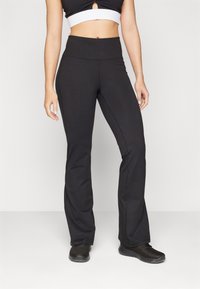 Black flared pants made of stretchy fabric with a high waist. Features include side seams and a smooth texture, paired with black athletic shoes.