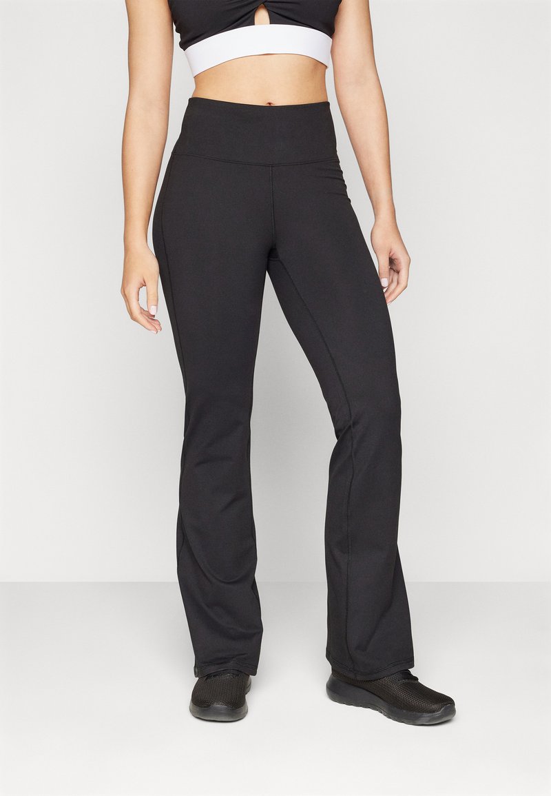 Black flared pants made of stretchy fabric with a high waist. Features include side seams and a smooth texture, paired with black athletic shoes.