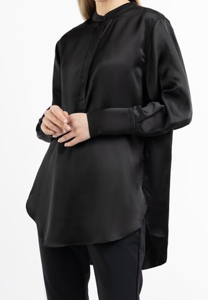Camicia nera in satin a maniche lunghe con colletto alla cinese, fessure laterali e vestibilità morbida, caratterizzata da una texture liscia e un orlo leggermente curvo.