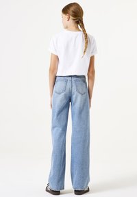 Top blanco de manga corta y jeans de pierna ancha de talle alto en azul claro. Los jeans cuentan con bolsillos traseros y una textura de denim clásica.