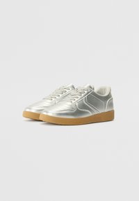 Silberne metallische Sneaker mit glatter Oberfläche, versehen mit Schnürsenkeln, runder Zehenpartie, weißen Akzenten und einer sandfarbenen Gummisohle.