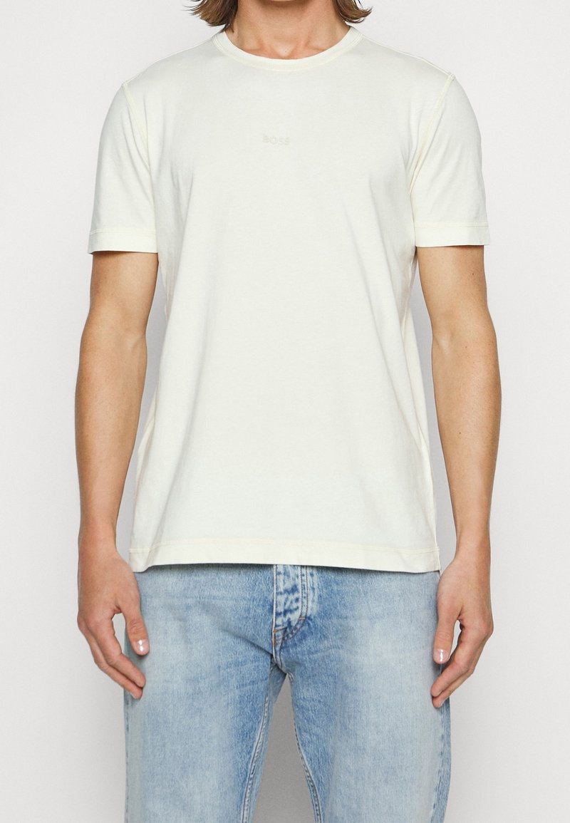 Krótki rękaw, kremowa koszulka wykonana z bawełny. Posiada okrągły dekolt i subtelne logo "BOSS" na środku. Gładka faktura.