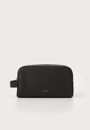 Trousse de toilette en cuir texturé noir avec une poignée sur le côté et un petit logo "Calvin Klein" centré à l'avant.