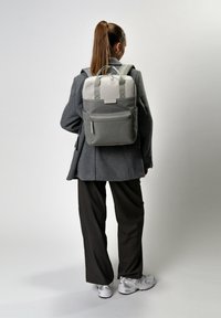 Mochila gris con una parte superior de gris más claro, cuenta con dos asas para transporte, un bolsillo frontal con cremallera y correas ajustables. Material suave y duradero.