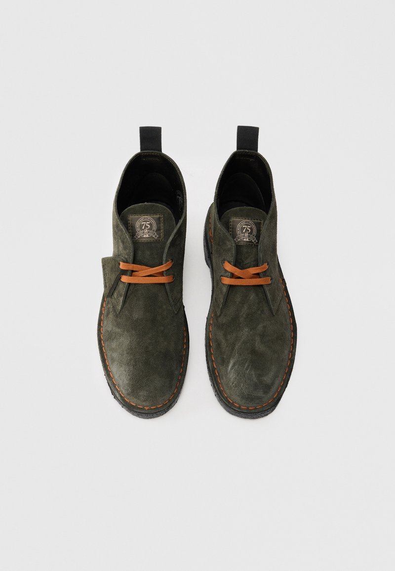 Pair of dark green suede desert boots with orange laces and stitching, black pull tabs, and a 75th anniversary label on the tongue.