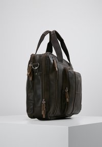 Braune Lederhandtasche mit mehreren Reißverschlusstaschen, zwei Griffen und einer glatten Textur. Verfügt über Akzente an den Reißverschlussanhängern. Seitenansicht.