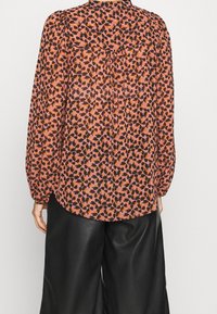 Genomskinlig, mönstrad blus med rosa och svart design, med långa ärmar, en bakfåll och en rundad nederkant. Matchad med svarta läderbyxor.