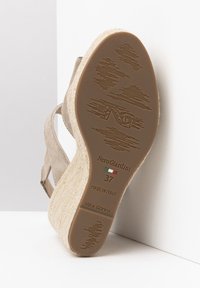 Beige wedge sandal with fabric straps, textured soles, and embossed branding. Notable height with a natural jute-like finish on the heel.