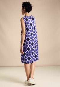 Ärmelloses Kleid in Lila mit einem geometrischen schwarz-weißen Muster; strukturierter Stoff, knielang, mit gerafftem Ausschnitt und lockerer Passform.