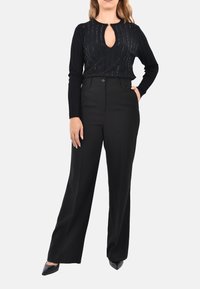 Top nero a maglia con texture verticale e dettaglio a forma di chiave, abbinato a pantaloni wide-leg neri a vita alta, completato da décolleté neri a punta.