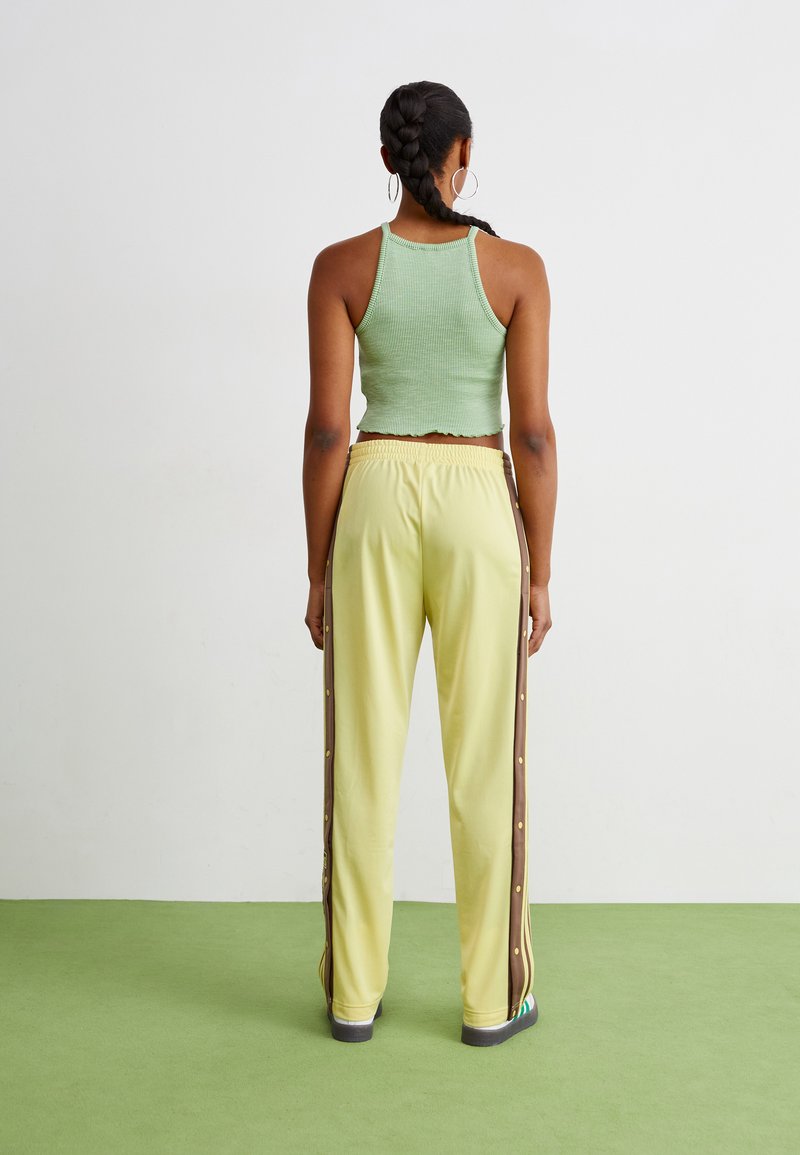 Zielony prążkowany top na brzuch połączony z żółtymi spodniami dresowymi z brązowymi paskami po bokach i guzikami snap. Model pokazany z tyłu.