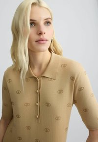 Gebreide poloshirt in beige, met een kraag, korte mouwen en knoopsluiting. Subtiel patroon van verweven cirkels door het hele shirt.