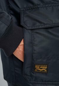Marineblauer Bomberjacke mit gerippten Bündchen, Seitentasche und einer aufgenähten Logopatch mit der Aufschrift "PME LEGEND" in goldenen Akzenten.