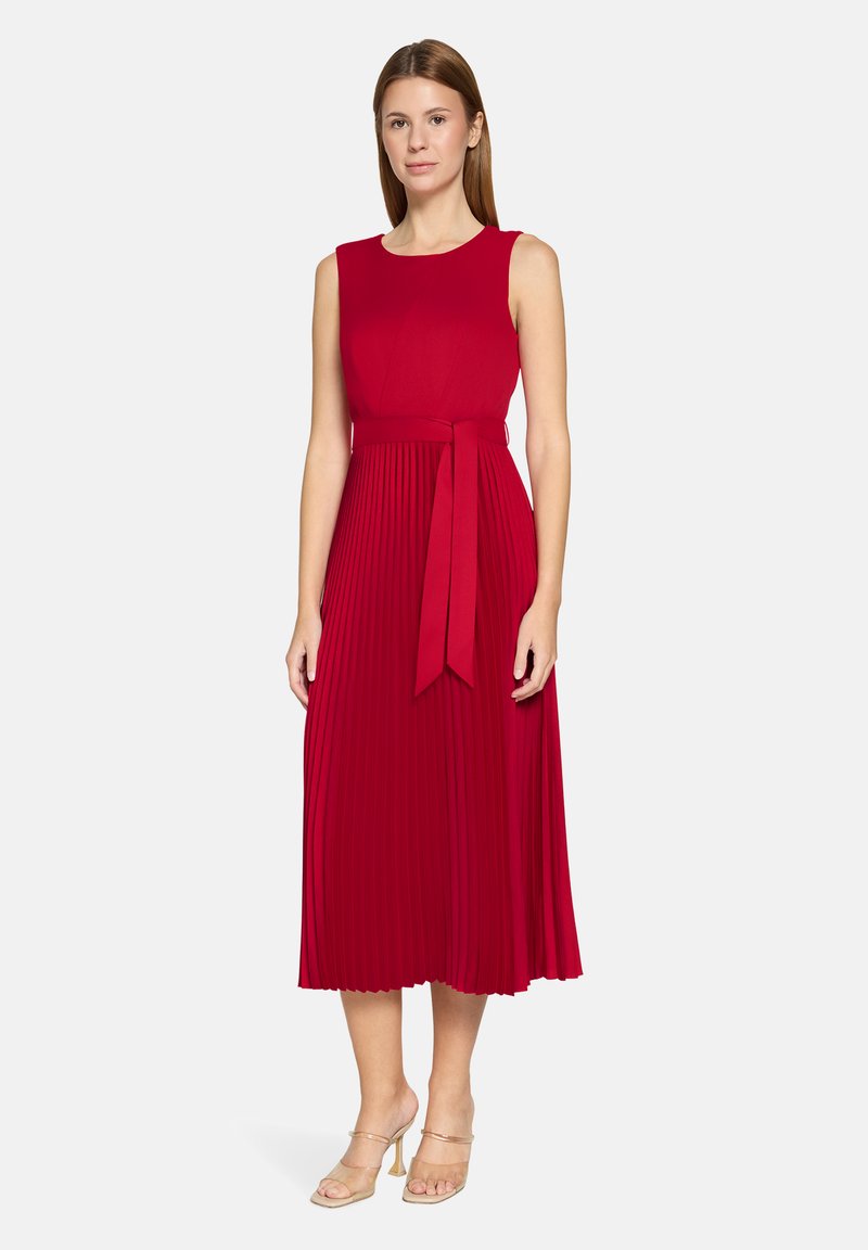 Robe rouge sans manches avec un corsage ajusté, une jupe plissée et une ceinture assortie nouée à la taille. Tissu lisse avec une silhouette fluide.