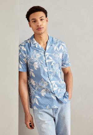 Camisa de manga corta azul con patrón floral blanco, cuello y botones en la parte delantera, combinada con jeans de mezclilla azul claro. Textura de tela suave.