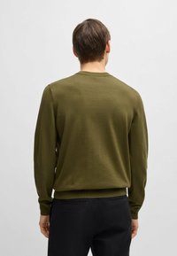 Khaki zielony sweter z długimi rękawami i okrągłym dekoltem, charakteryzujący się gładką strukturą i dopasowaną talią, w połączeniu z czarnymi spodniami.