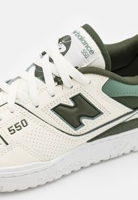 Gros plan sur une sneaker New Balance 550 blanche et verte avec des lacets blancs, un côté perforé et des détails de semelle et de languette avec logo.