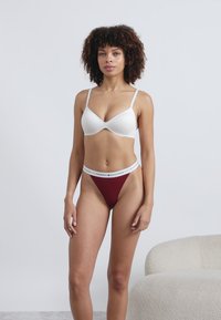 Hvit polstret bh med tynne stropper, kombinert med en burgunder tanga med en hvit merkevaremidjebånd. Glatt stofffinish.