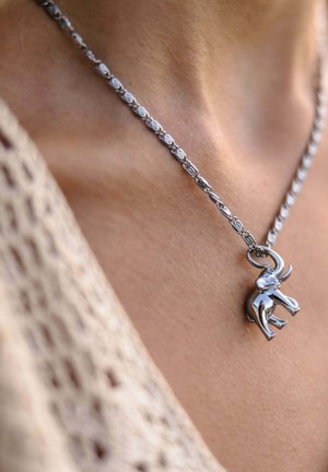 Silver chain necklace with a small elephant pendant worn on a person’s neck over tan skin and beige knit fabric.