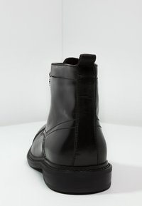 Černé kožené kotníkové boty s hladkým povrchem, s nízkým podpatkem a zádním poutkem. Detailní šití podél strany a podrážky.