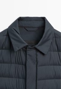 Dunkelblau gesteppte Jacke mit einem Schalkragen, Knopfverschluss und glatter Textur. Mit horizontaler Naht und minimalistisches Design.