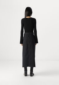 Black ribbed long-sleeve top paired with a high-waisted black denim maxi skirt featuring back pockets and frayed hem, complemented by black heeled boots.