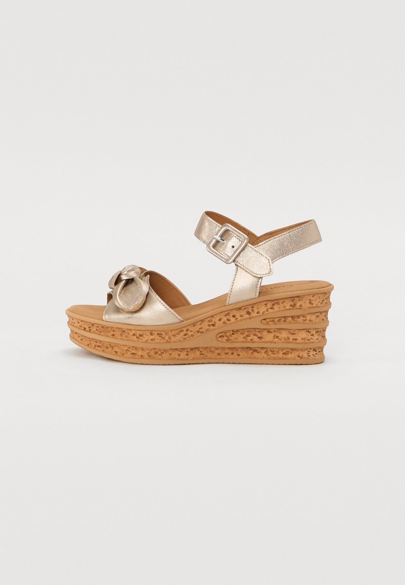 Golden wedge sandals with a textured cork platform, adjustable ankle strap, and a decorative bow detail on the upper.