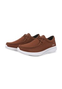 Scarpe slip-on in suede marrone con suola in gomma bianca. Presentano accenti cuciti e un minimo dettaglio di lacci. Logo laterale in bianco.