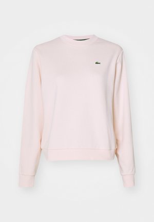 Hanorac roz deschis cu mâneci lungi, guler și tiv cu nervuri. Prezintă un mic logo brodat verde în zona stângă a pieptului.