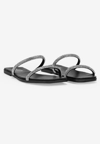 Sandalias planas negras con dos tiras adornadas con cristales, que presentan un acabado mate suave y un diseño minimalista. Estilo ligero y de punta abierta.