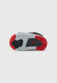 Semelle de chaussure de sport noire et grise avec des accents rouges ; elle présente des motifs texturés, des rainures et un logo bien en vue.