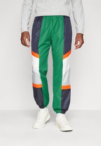 Kleurige sportbroeken met groene, marineblauwe en witte panelen en oranje accenten. Gemaakt van lichtgewicht materiaal met elastische boorden.