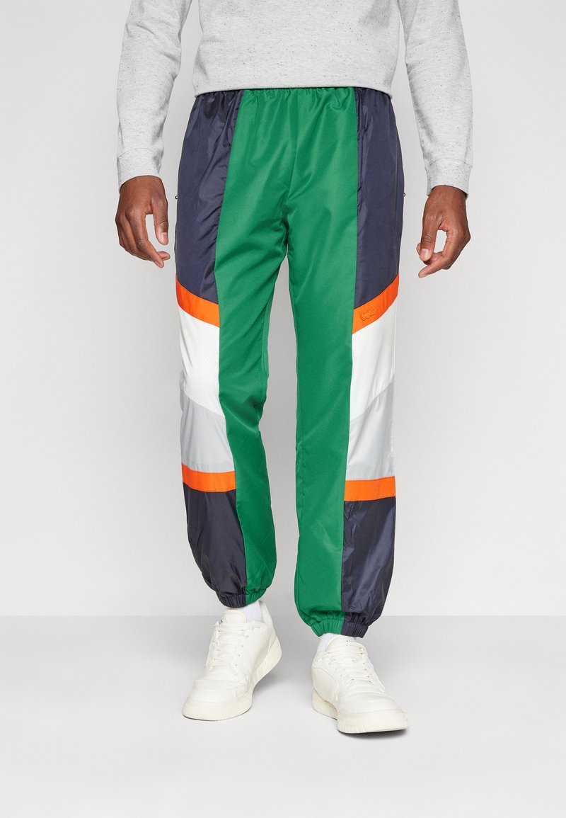 Kleurige sportbroeken met groene, marineblauwe en witte panelen en oranje accenten. Gemaakt van lichtgewicht materiaal met elastische boorden.