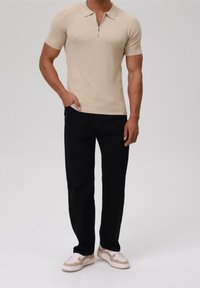 Beige ribbad kortärmad polo med dragkedja i kragen, kombinerad med svarta byxor och ljusa sneakers med beige detaljer.