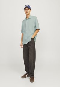 Lys grøn kortærmet skjorte med et struktureret mønster, parret med løstsiddende mørkebrune jeans og brune sneakers med hvide detaljer.
