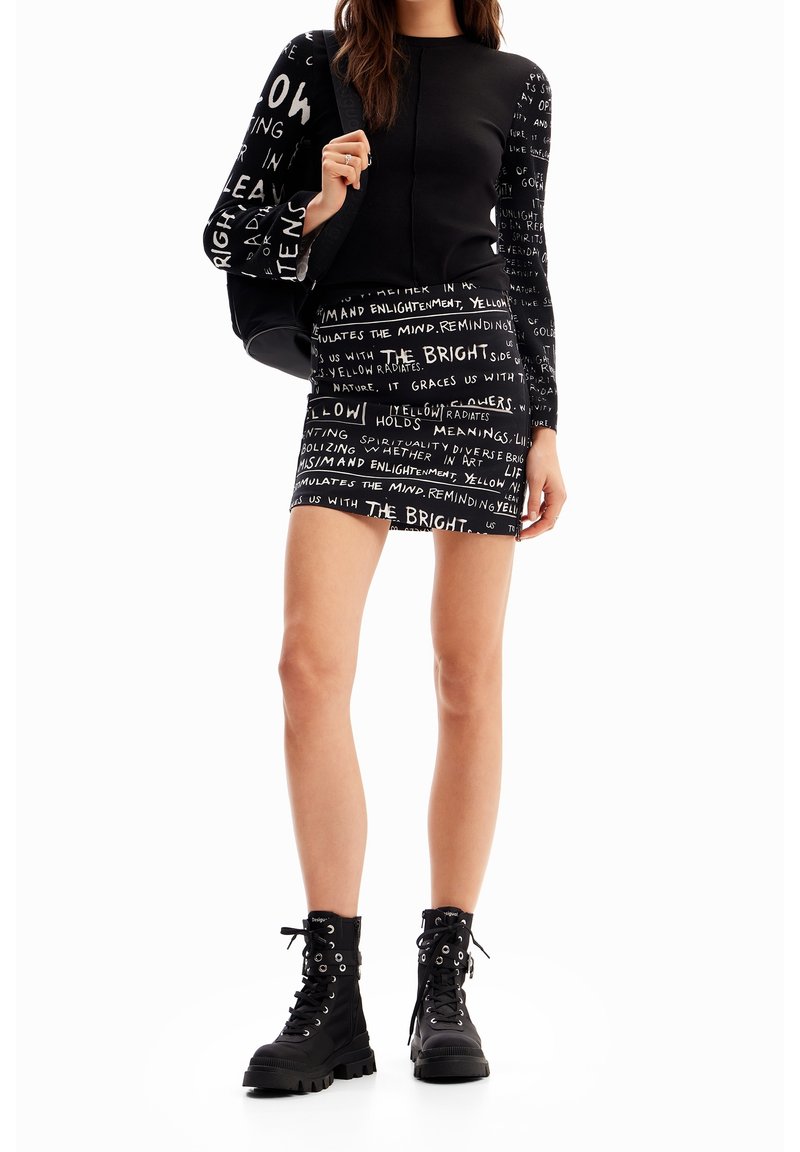 Svart långärmad topp med grafisk text, matchad med en mini kjol. Utrustad med svarta kängor med öglor och snören.