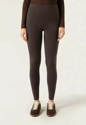 Leggings noirs taille haute avec une texture lisse, un design ajusté et sans coutures visibles, associés à des chaussures de sport sombres avec des lacets clairs.