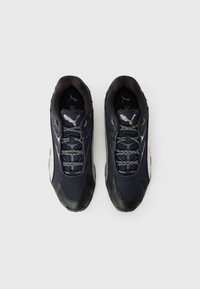 Marineblå sneakers med sorte gummisåler, tekstureret stofoverdel, reflekterende detaljer og mønstrede snørebånd. Puma-logo ved hælen og på tungen.
