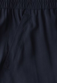 Marineblauwe broeken met een elastische tailleband, voorzien van een platte voork pockets en een gladde, gestructureerde stof. Stikseldetails zichtbaar.