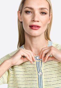 Knit cardigan in yellow and blue with horizontal stripes, featuring a round neckline and two buttons at the front. Texture appears soft.