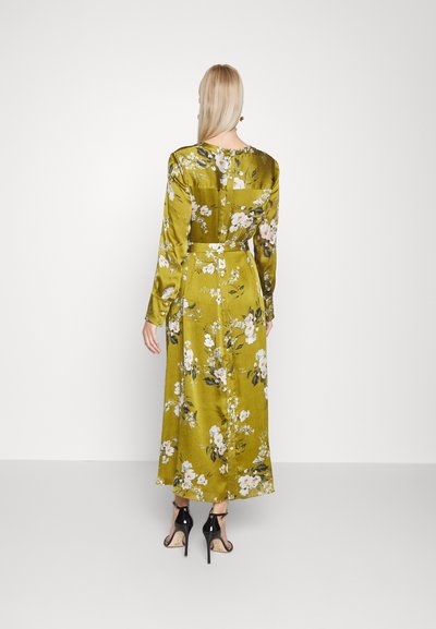 Vestido maxi florido em cetim verde oliva, com mangas longas, cintura com cinto e fecho de botão deslizante nas costas. Stilettos pretos.