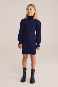 Tengerés ribbed kötött ruha magas garbóval, puffos ujjal és testhezálló sziluettel. Fekete bokacsizmával párosítva.