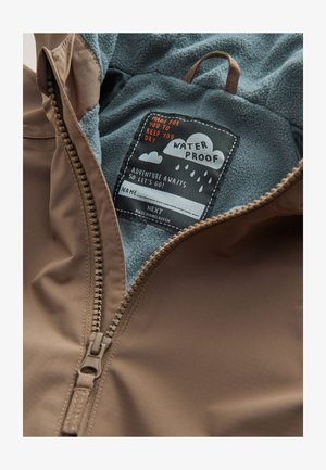 Bruine waterdichte jas met een zachte blauwe fleece voering aan de binnenkant en een waslabel met afbeeldingen, waaronder wolken en regendruppels.