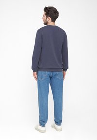Dunkelblaue Sweatshirt mit gerippten Bündchen und Saum, kombiniert mit hellblauen Jeans, von hinten betrachtet. Legere Schuhe runden den Look ab.