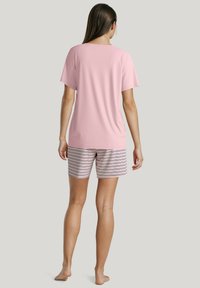 Lichtroze top met korte mouwen, gecombineerd met gestreepte shorts in wit, roze en marineblauw. Zacht materiaal met een ontspannen pasvorm, getoond vanuit de achterkant.