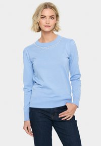 Maglione a maglia blu chiaro con maniche lunghe, orlo a costine e scollo rotondo decorativo con accenti di perline. Abbinato a jeans scuri.