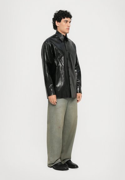 Svart, blank knäpp skjorta med långa ärmar, kombinerad med lösa, ljusgröna denimbyxor och svarta skor. Modellen står mot en vit bakgrund.