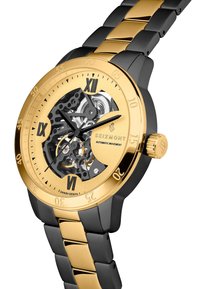 Gull og svart automatisk klokke med transparent urskive som viser indre mekanismer og romerske tall. Har et to-tonet metalarmbånd.