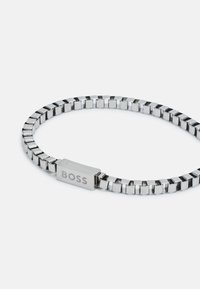 Bracelet en métal présentant des maillons rectangulaires au fini argent poli, avec un fermoir rectangulaire gravé de "BOSS".